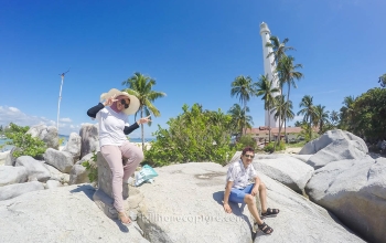 Pasangan berdiri di pantai Belitung latar belakang mercusuar pulau lengkuas